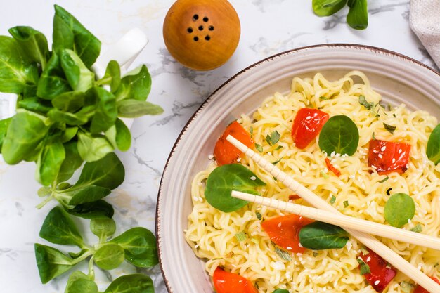 Fideos con pimienta, hojas de lechuga y semillas de sésamo en un plato de cerámica y palillos, vista superior