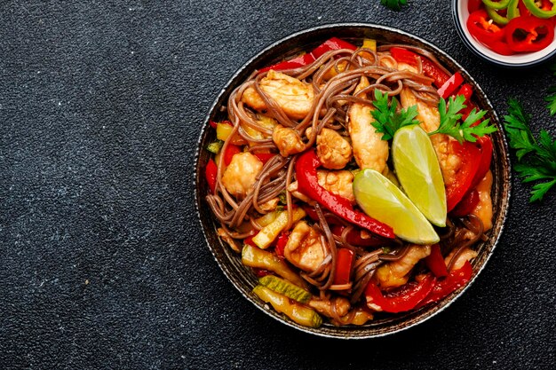 Fideos salteados de cocina asiática con pollo y verduras y semillas de sésamo en un tazón Espacio de copia de vista superior de fondo de mesa de cocina negra