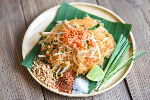 Fideos salteados Pad Thai en un plato servido en la mesa del comedor, comida tailandesa, fideos fritos al estilo tailandés con gambas, brotes de soja y guarnición de cacahuetes, chile en polvo, azúcar, lima limón - vista superior