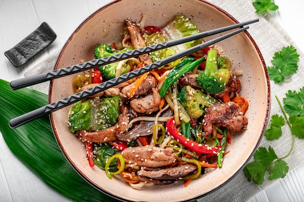 Fideos salteados udon con carne de cerdo y verduras en un plato sobre fondo blanco de madera