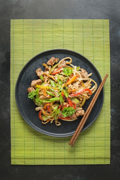 Fideos salteados udon con tazón de cerdo y palillos sobre fondo de piedra negra cocina asiática