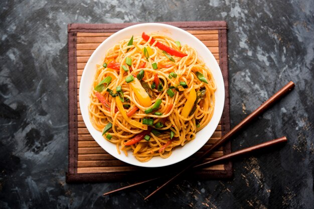 Los fideos Schezwan o los fideos Hakka de verduras o chow mein son recetas populares indochinas, que se sirven en un tazón o plato con palillos de madera. enfoque selectivo