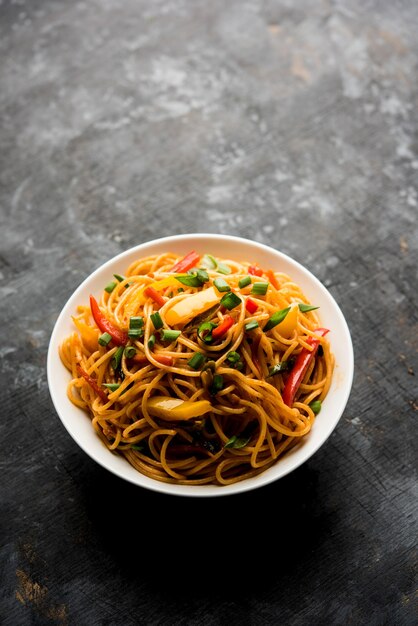 Los fideos Schezwan o los fideos Hakka de verduras o chow mein son recetas populares indochinas, que se sirven en un tazón o plato con palillos de madera. enfoque selectivo