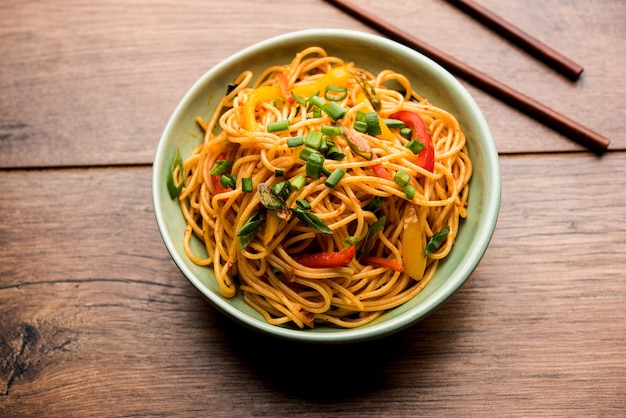 Los fideos Schezwan o los fideos Hakka de verduras o chow mein son recetas populares indochinas, que se sirven en un tazón o plato con palillos de madera. enfoque selectivo