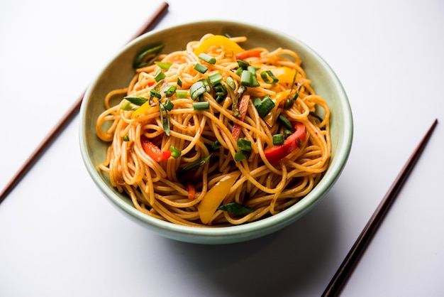 Los fideos Schezwan o los fideos Hakka de verduras o chow mein son recetas populares indochinas, que se sirven en un tazón o plato con palillos de madera. enfoque selectivo