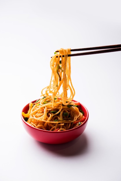 Los fideos Schezwan o los fideos Hakka de verduras o chow mein son recetas populares indochinas, que se sirven en un tazón o plato con palillos de madera. enfoque selectivo