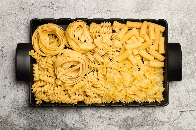 Fideos secos surtidos en una fuente rectangular negra con asas