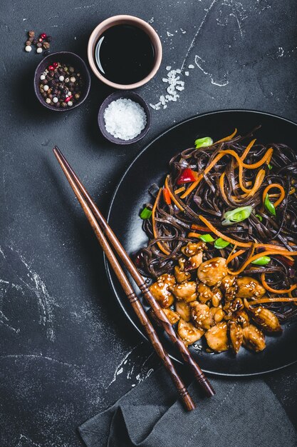 Fideos soba asiáticos, pollo, verduras, fondo oscuro de hormigón rústico.