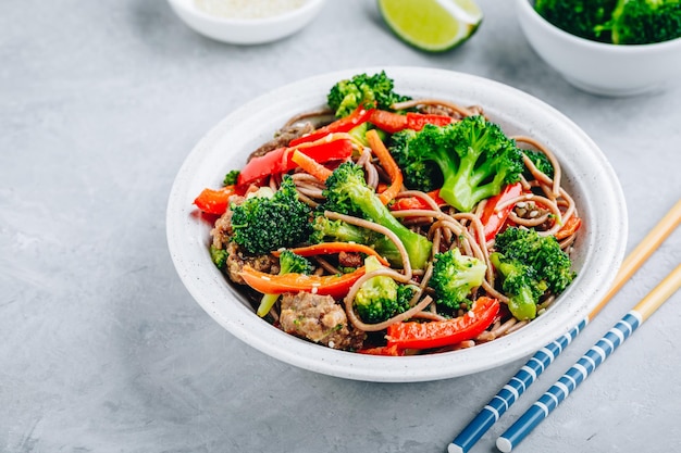 Fideos de ternera salteados con brócoli, zanahorias y pimientos rojos sobre fondo de piedra gris