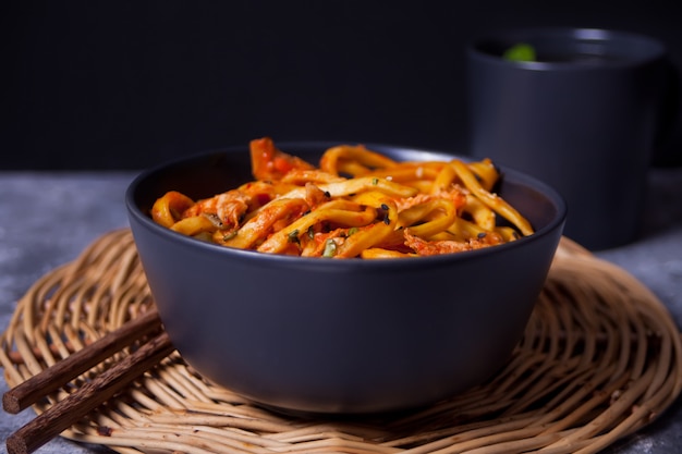 Fideos Udon con carne de pollo en un tazón sobre fondo de piedra oscura.