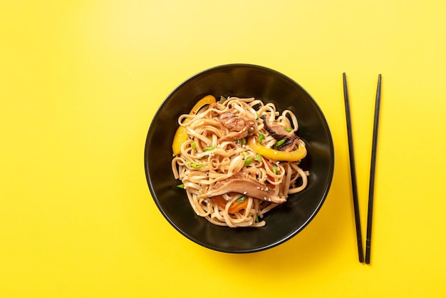 Fideos udon de comida asiática con pollo en un plato negro