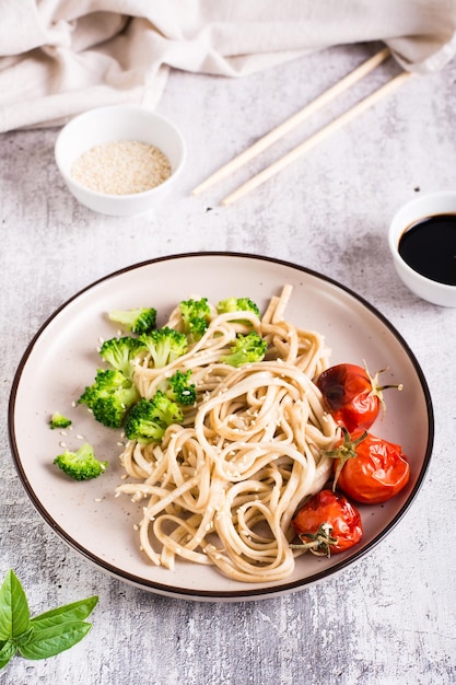 Fideos udon fritos en salsa de soja con tomates, brócoli y semillas de sésamo en un plato Vista vertical