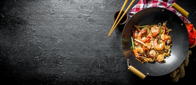 Foto fideos udon terminados en una sartén wok con palillos de salsa de soja y una servilleta