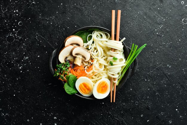 Fideos udon tradicionales japoneses Tazón de fideos con champiñones de huevo cebollas verdes Sobre un fondo negro Vista superior