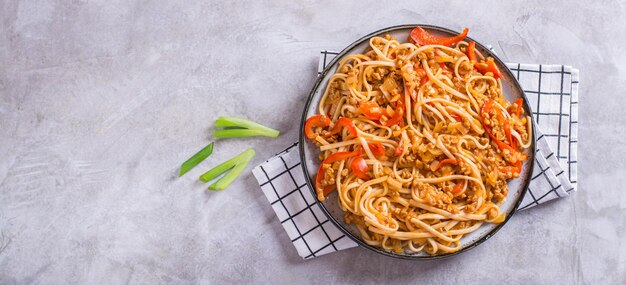 Fideos vegetarianos con pimientos de carne de soja y tomates en un plato en el banner web de la vista superior de la mesa