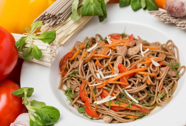 Fideos con verduras y guarnición en plato blanco