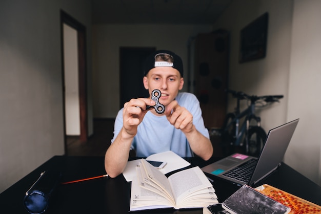 Fidget Spinner en manos de un joven sentado en su habitación en el escritorio. Concéntrate en el giro.