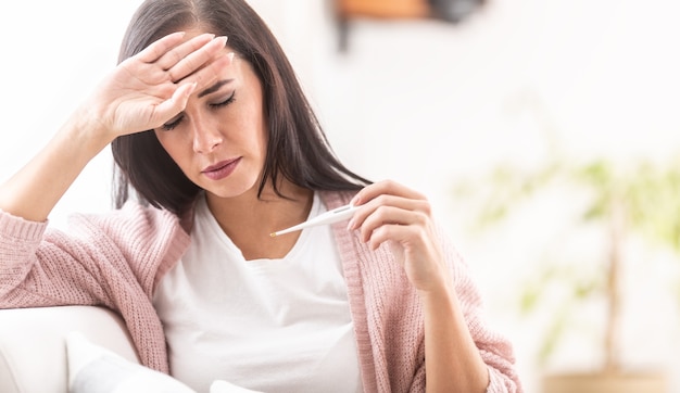 Fiebre que la mujer mide la temperatura con un termómetro estándar.