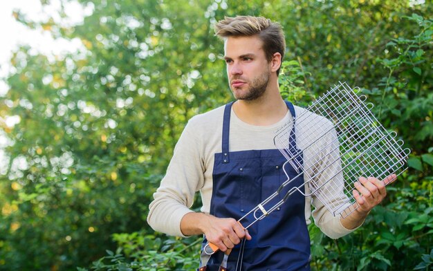 Fiesta de barbacoa en el patio trasero Herramientas para asar carne al aire libre Concepto de picnic Chico guapo cocinando comida Comida saludable Parrilla de recetas Diferentes métodos para asar El hombre sostiene la rejilla para asar Comida a la parrilla