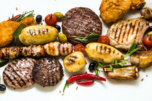 Fiesta de carne a la barbacoa con diferentes tipos de carne: hamburguesas de ternera, costillas de cerdo, albóndigas de pavo, muslos de pollo empanizados con papas y tomates, especias y hierbas aromáticas. Menú de verano