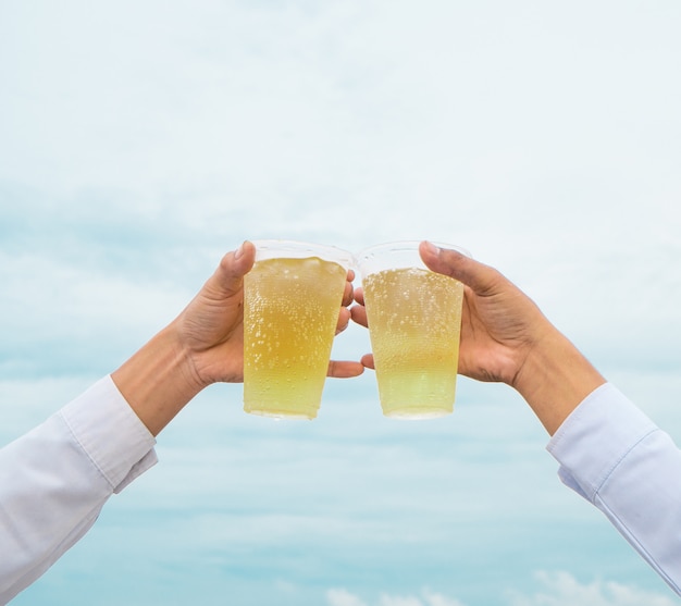 Fiesta de celebración, las manos sostienen cervezas de bebidas con vasos de plástico y animan al éxito con un hermoso cielo como fondo