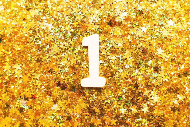 Foto fiesta de cumpleaños de un año número uno con confeti dorado en forma de estrellas sobre fondo amarillo