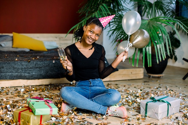 Fiesta de cumpleaños, carnaval de año nuevo. mujer sonriente africana joven que celebra evento brillante ,. confeti chispeante, divertirse, bailar y beber champán