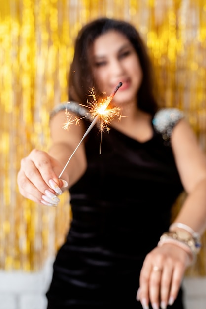 Foto fiesta de cumpleaños. hermosa joven sosteniendo bengala y globo sobre fondo dorado