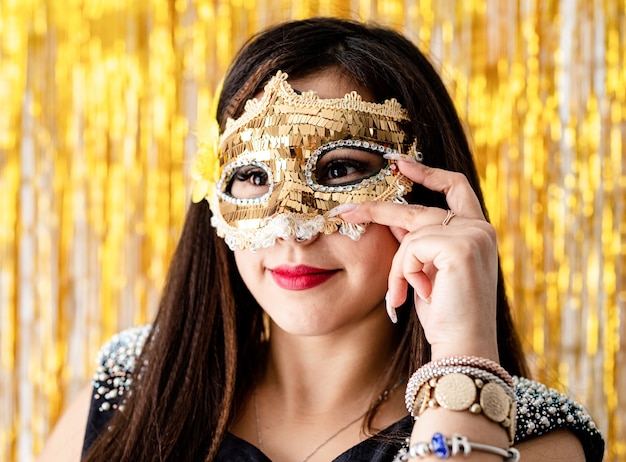 Fiesta de cumpleaños. Hermosa mujer morena en vestido de fiesta negro con máscara de mascarada de oro brillante