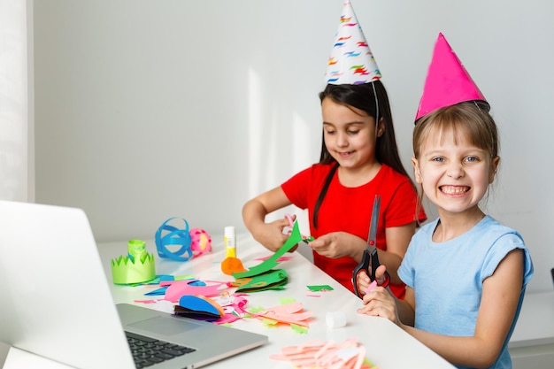 Fiesta de cumpleaños en línea para niños. Niñas en vestidos, sombrero celebran la fiesta con amigos. Conferencia, videollamada en laptop, computadora. Cuarentena, coronavirus pandémico covid-19.