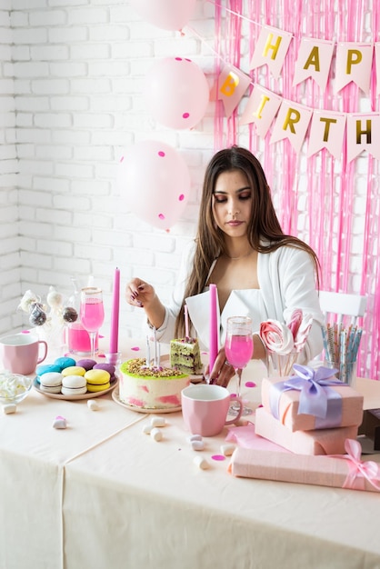 Fiesta de cumpleaños Mesas de cumpleaños Mujer atractiva en ropa de fiesta blanca preparando mesa de cumpleaños con pasteles cakepops macarons y otros dulces bebiendo