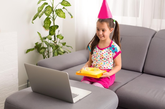 Fiesta de cumpleaños virtual para niños con pastel en línea junto con su amiga en videoconferencia. Con teléfono digital para una reunión en línea. Chica celebrando cumpleaños online en tiempo de cuarentena