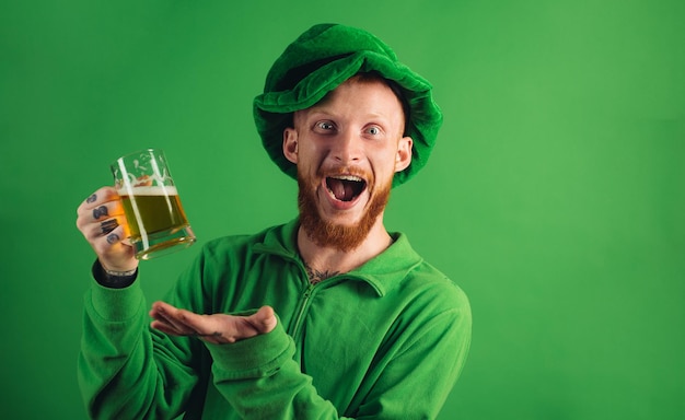 Fiesta del día de patricio retrato de hombre emocionado sosteniendo un vaso de cerveza en el día de san patricio aislado en verde...