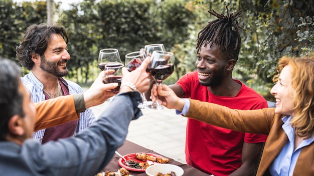 Fiesta familiar con padres adoptivos e hijos para celebrar los logros del joven estudiante de ascendencia africanapersonas de edades mixtas brindando con copas de vino tinto en la barbacoa