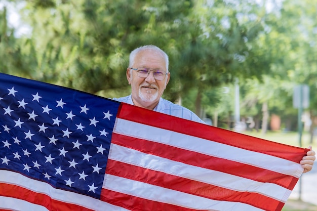 Fiesta federal estadounidense, feliz patriota senior vistiendo un barras y estrellas una gran bandera estadounidense en el día de la independencia