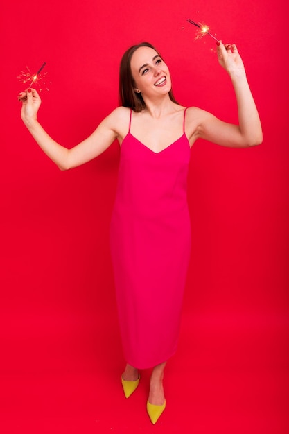 Fiesta de Nochevieja Una mujer joven con un vestido rosa sostiene bengalas de buen humor