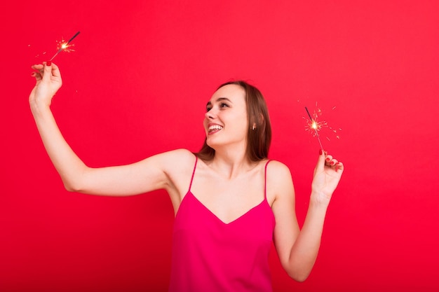 Fiesta de Nochevieja Retrato de una mujer joven con un vestido rosa sosteniendo bengalas de buen humor