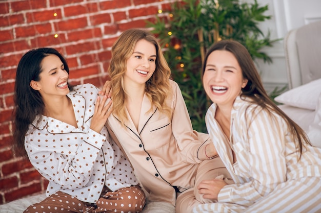 Fiesta de pijamas. Tres chicas guapas en pijama sentado en una cama y riendo