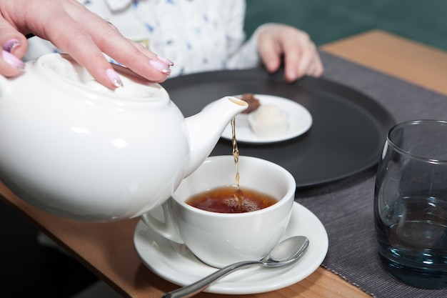 Fiesta del té familiar. El té negro se vierte en una taza de té con una tetera blanca. De cerca.