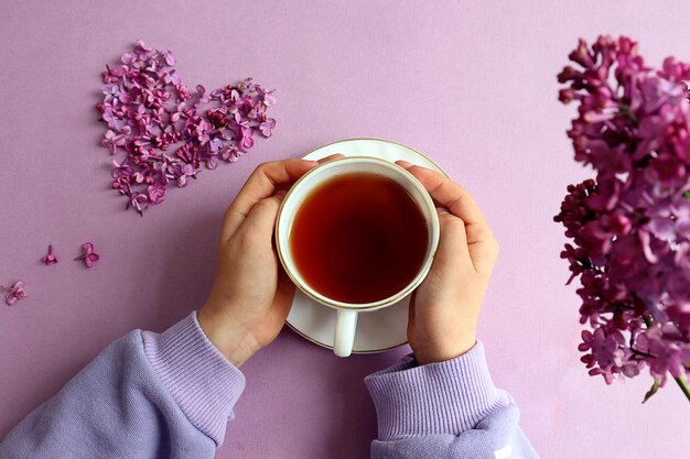 Fiesta del té de primavera una taza de té en las manos sobre un fondo pastel un corazón de flores lilas una rama lila cerca de la vista superior