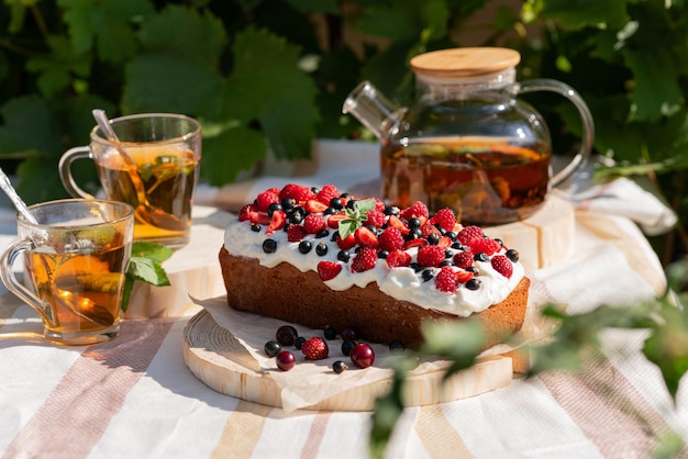 Fiesta de té de verano al aire libre con pastel casero o cupcake con bayas y té de menta con crema batida para dos personas Bodegón de verano