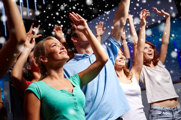 Foto fiesta, vacaciones, celebración, vida nocturna y concepto de la gente - amigos sonrientes saludando con la mano en un concierto en el club y el efecto de la nieve