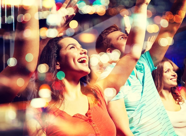 Foto fiesta, vacaciones, celebración, vida nocturna y concepto de la gente - amigos sonrientes saludando con la mano en un concierto en el club