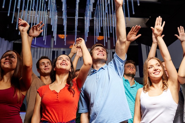 fiesta, vacaciones, celebración, vida nocturna y concepto de la gente - grupo de amigos sonrientes saludando con la mano en un concierto en el club