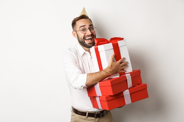 Fiestas y celebraciones. Hombre emocionado tener fiesta de cumpleaños y recibir regalos, mirando feliz, de pie sobre fondo blanco.