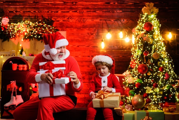 Foto fiestas familiares y infancia santa claus y pequeño ayudante de santa con regalo en la habitación decorada para