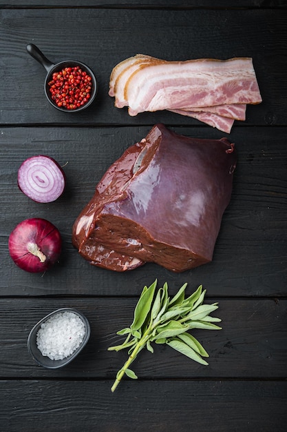 Fígado bovino com bacon e cebola em fundo preto de madeira, vista superior.