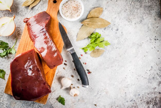 Fígado de bovino cru com especiarias, ervas e legumes, vista de mesa de pedra cinza