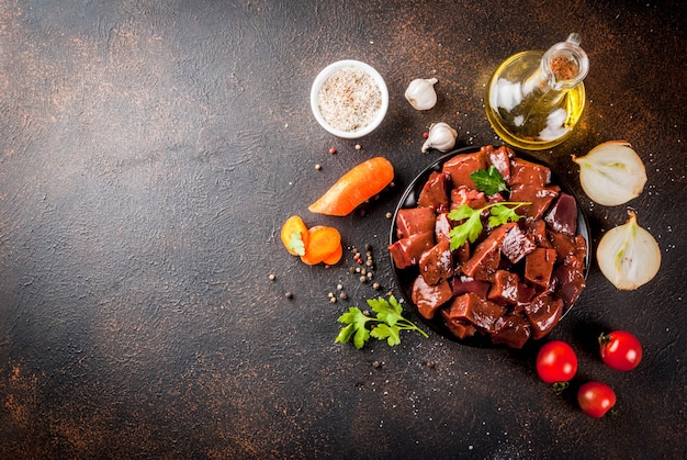 Fígado de bovino cru fatiado com especiarias, ervas e legumes, vista de mesa enferrujada escura