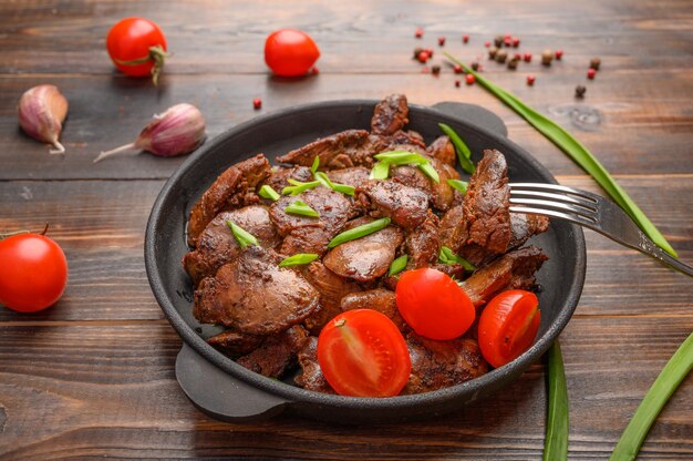 Fígado de frango caseiro frito com molho de soja, tomate, cebola e especiarias na mesa de madeira. fatia de picada num garfo. comida saudável.